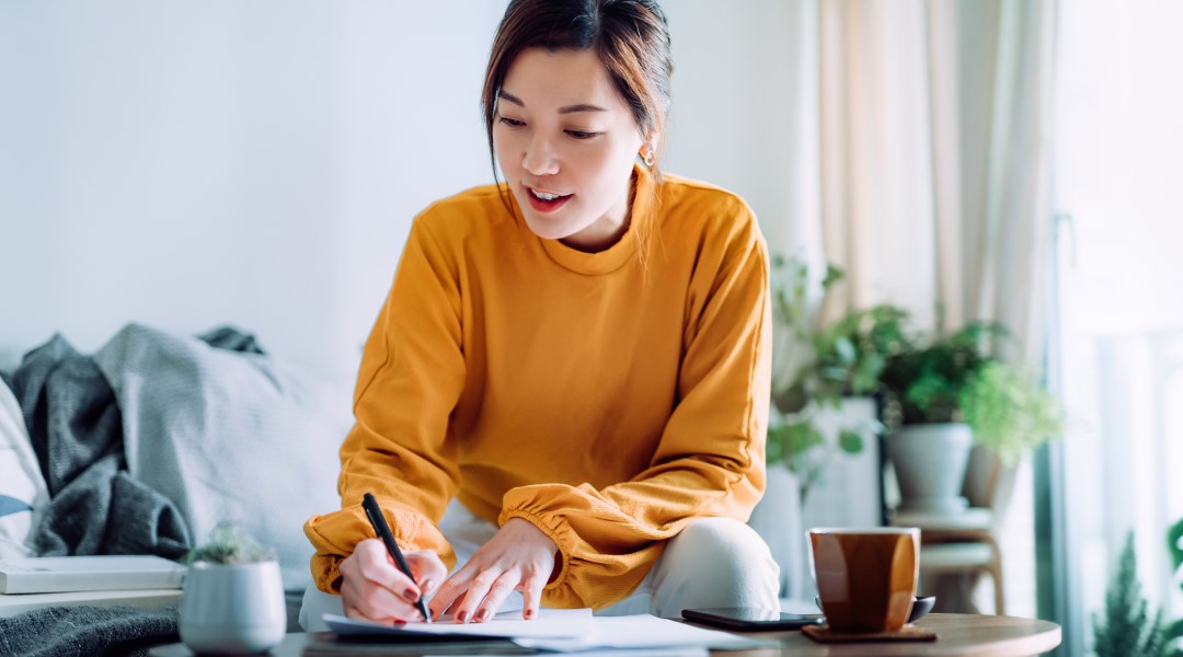 Lady writing on the coffee able with a pen and paper